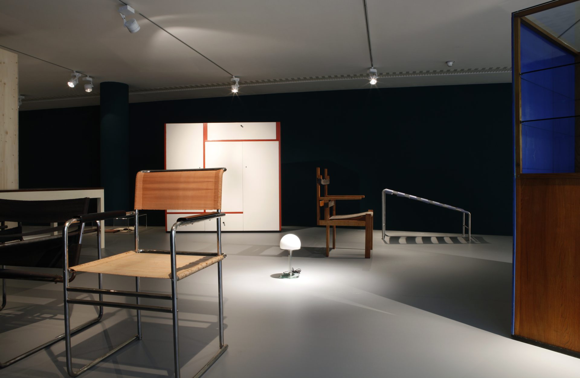 Exhibition view. Chairs, cupboards, table, lamp and lounger arranged on a pedestal