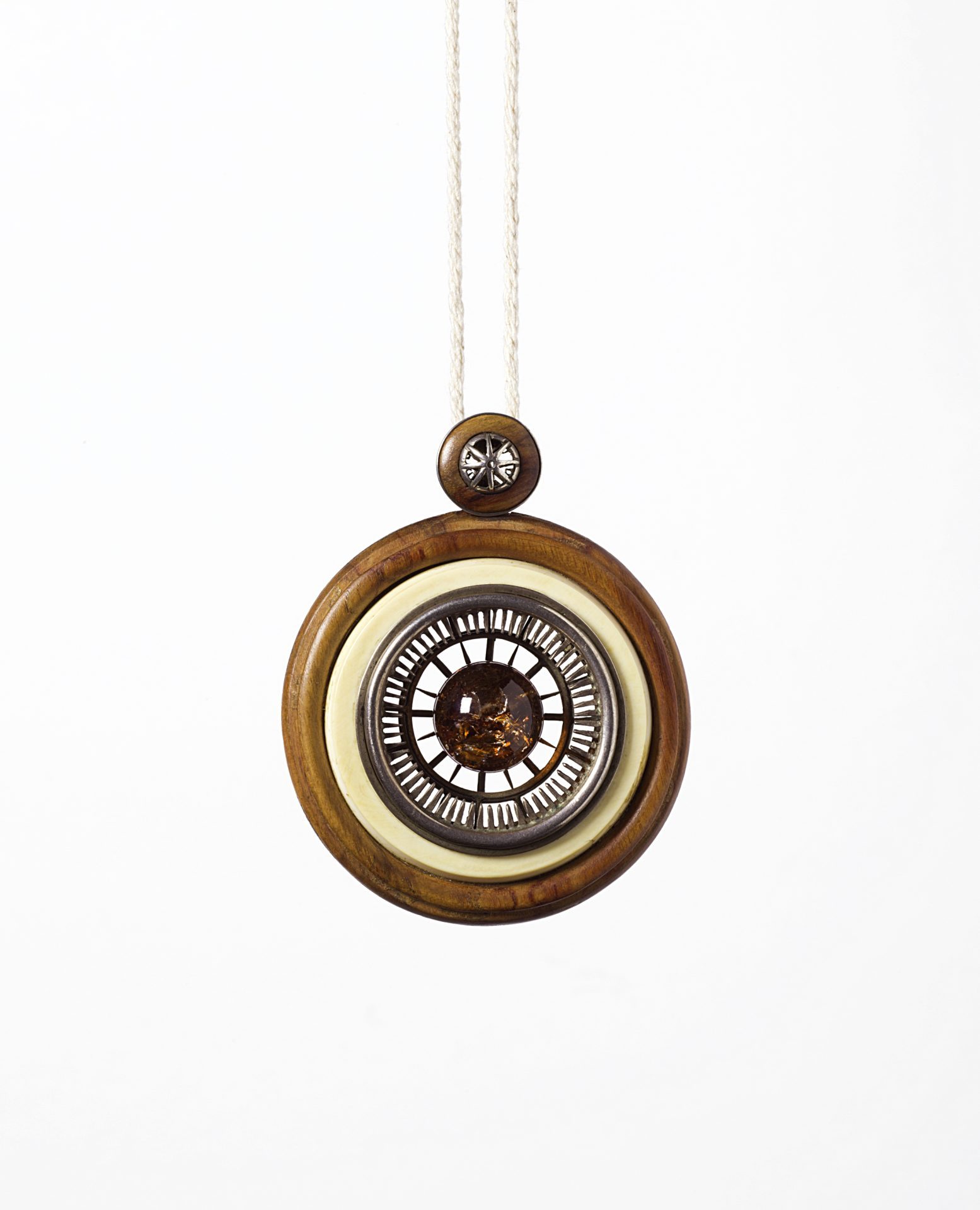 Pendant with central brownish gemstone, inserted in a setting of (from the outside in): Rosewood, ivory and a fine silver setting. Attached to a simple cord typical of the period. Characteristic is its structure of concentric circles.