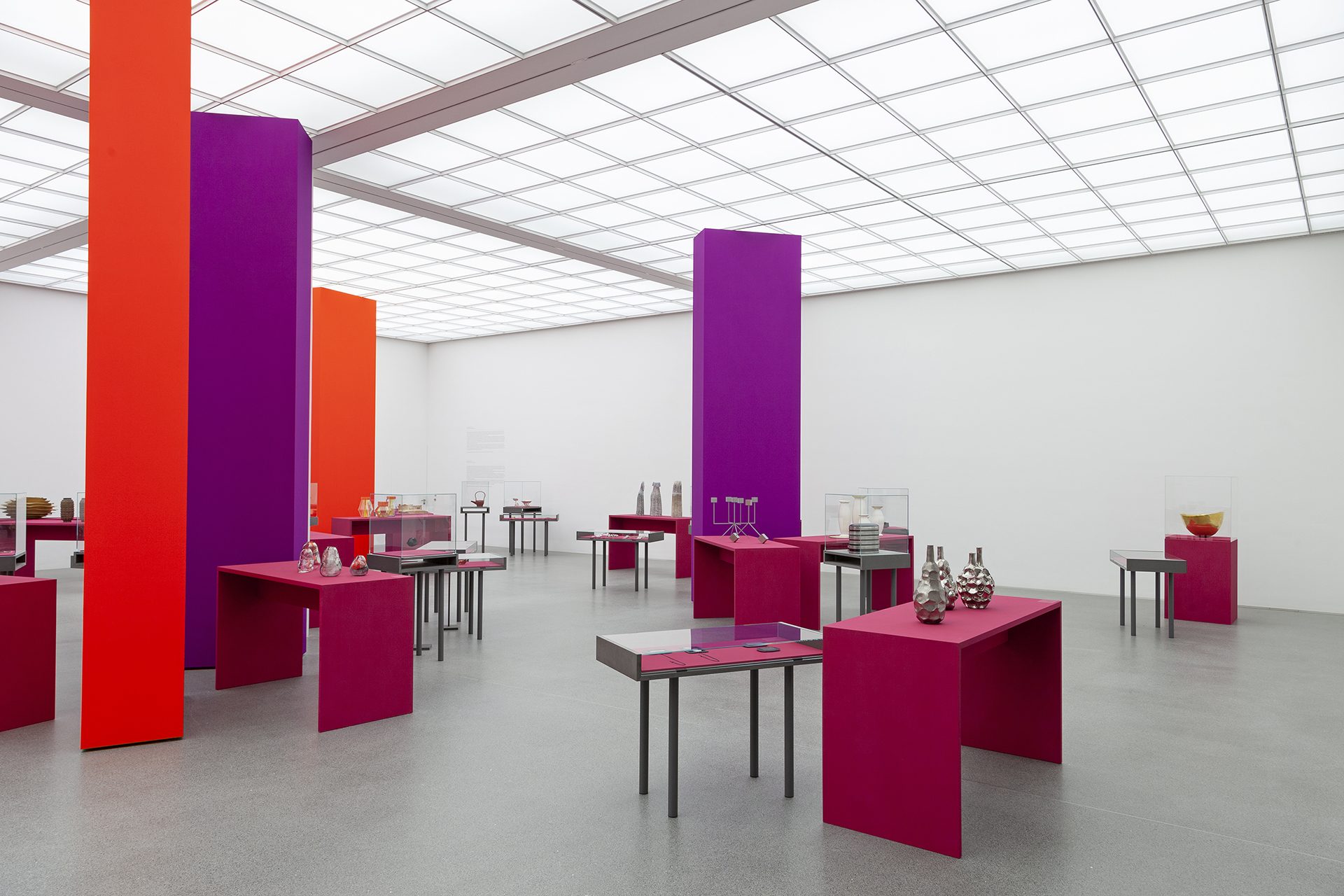 Blick in die Ausstellung "Danner-Preis 2020. 100 Jahre Danner-Stiftung", rote und lila Säulen im Raum, auf pinken Podesten/ Vitrinen sind die Objekte ausgestellt.