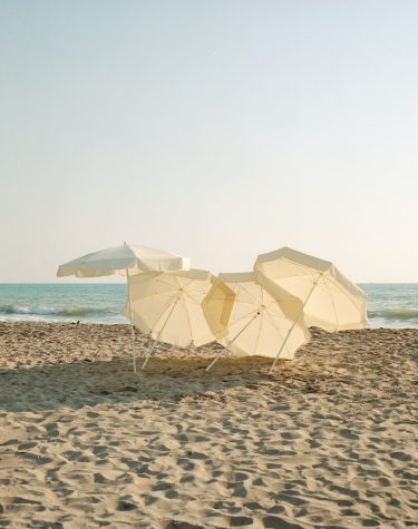 4 aufgespannte blassgelbe Sonnenschirm am Strand. Der linke steht aufrecht, die anderen neigen sich stark zu Boden.