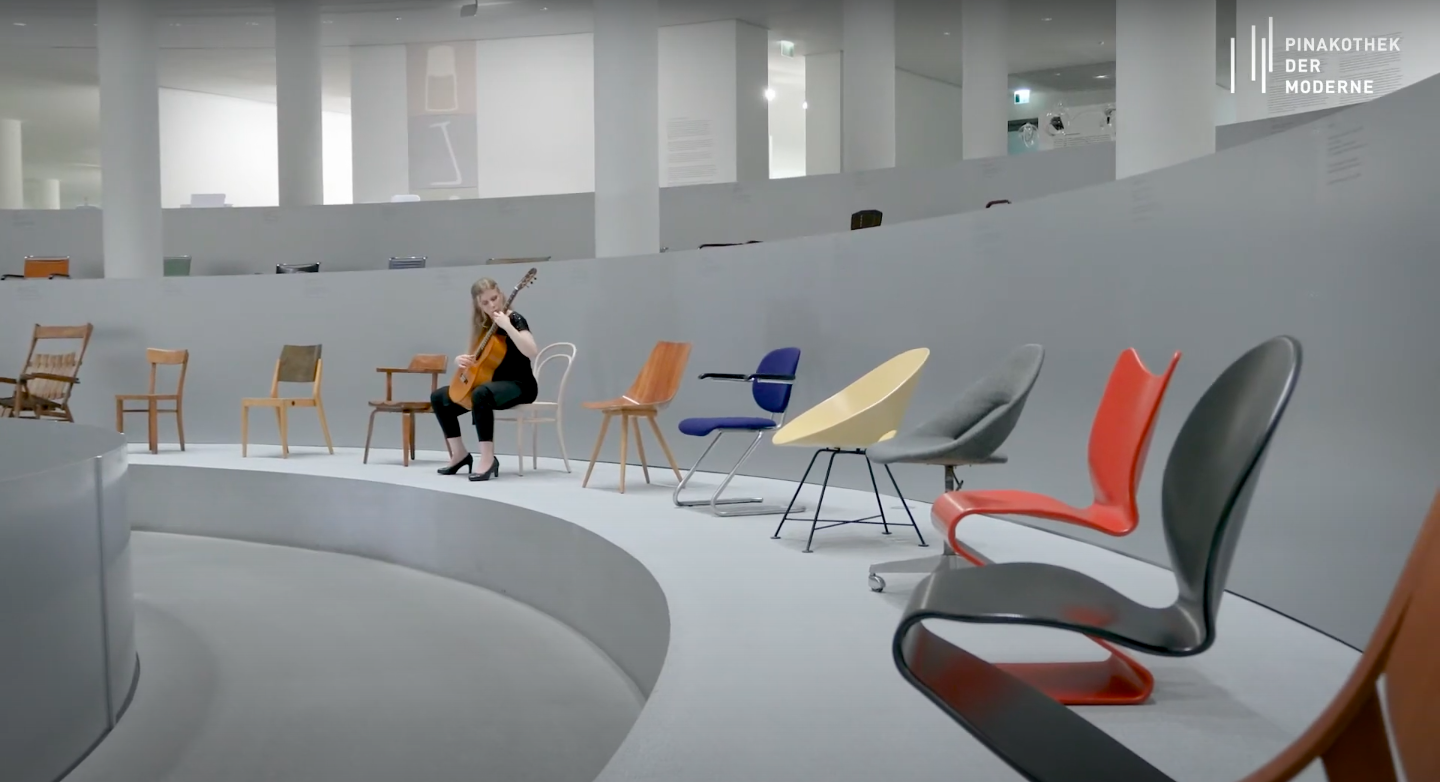 Laura Lootens mit ihrer Gitarre auf den Stühlen der Ausstellung "Thonet & Design" in der Rotunde sitzend.