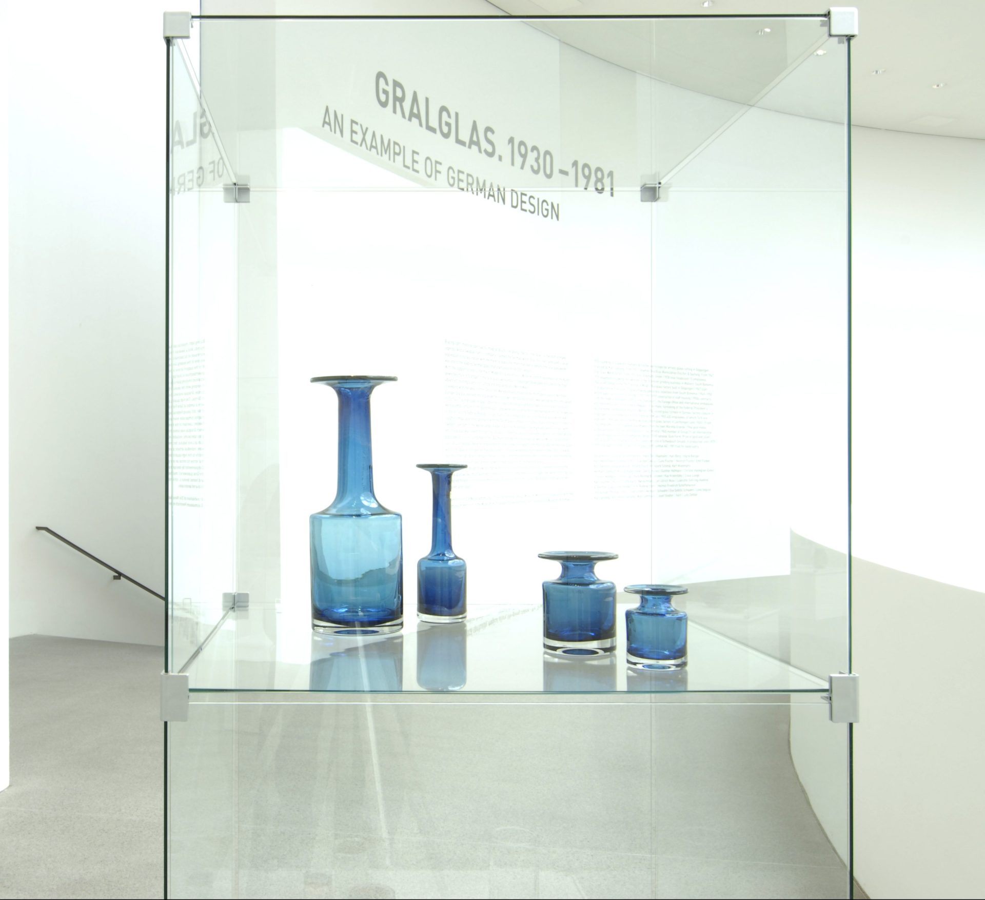 Blick in eine Glasvitrine mit vier blauen Glasvasen: zylindrisch, mit eingezogenen Schultern und zylindrischen, unterschiedlich langen Hälsen.