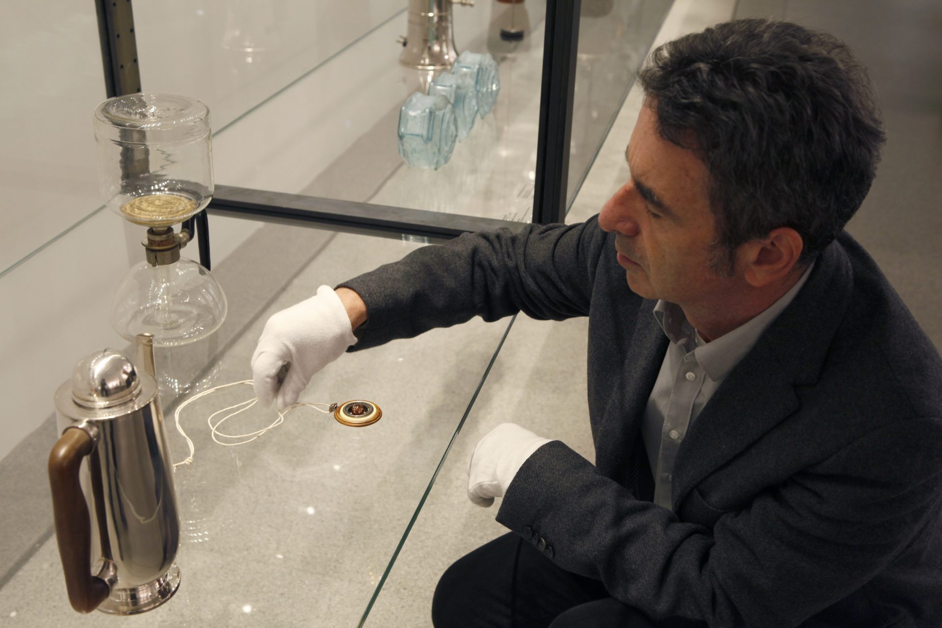 Dr. Josef Strasser adds the Bauhaus pendant to the glass display case. There are already other objects inside the showcase.