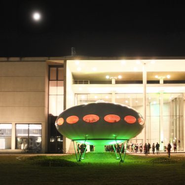 Exterior view of the Futuro at night in front of the Pinakothek der Moderne.