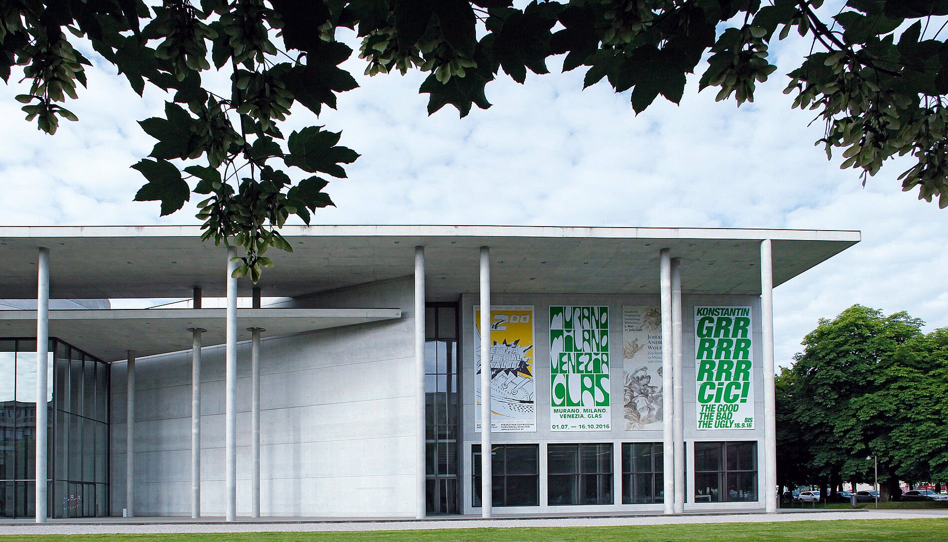 Aussenansicht der Pinakothek der Moderne mit 4 Bannern der 4 Museen. Rechts das Banner für die Ausstellung "The Good, The Bad, The Ugly" in der Neuen Sammlung, grün auf weiß.