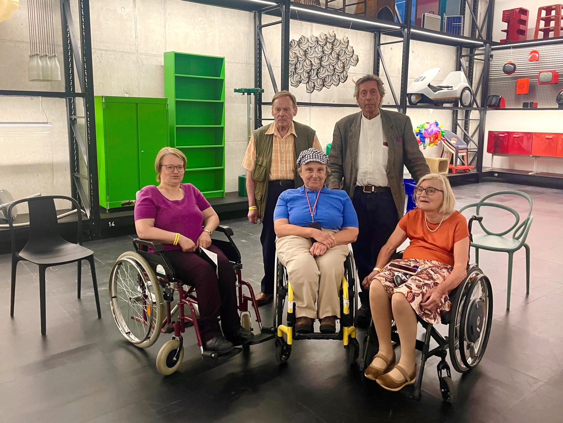 Group photo in front of the shelves in the X-D-E-P-O-T. Three women in wheelchairs form the front row. Behind them two men are standing.