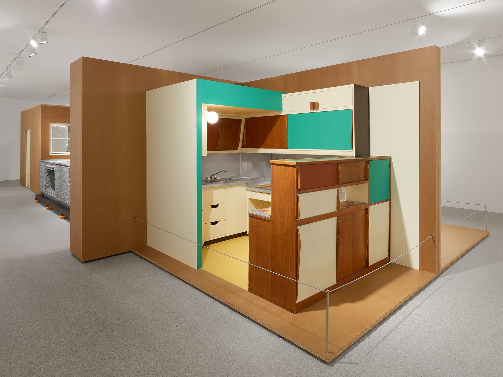 You can see the exhibition installation “Kitchen Culture” consisting of brown wall and floor elements in which various kitchens are set up.