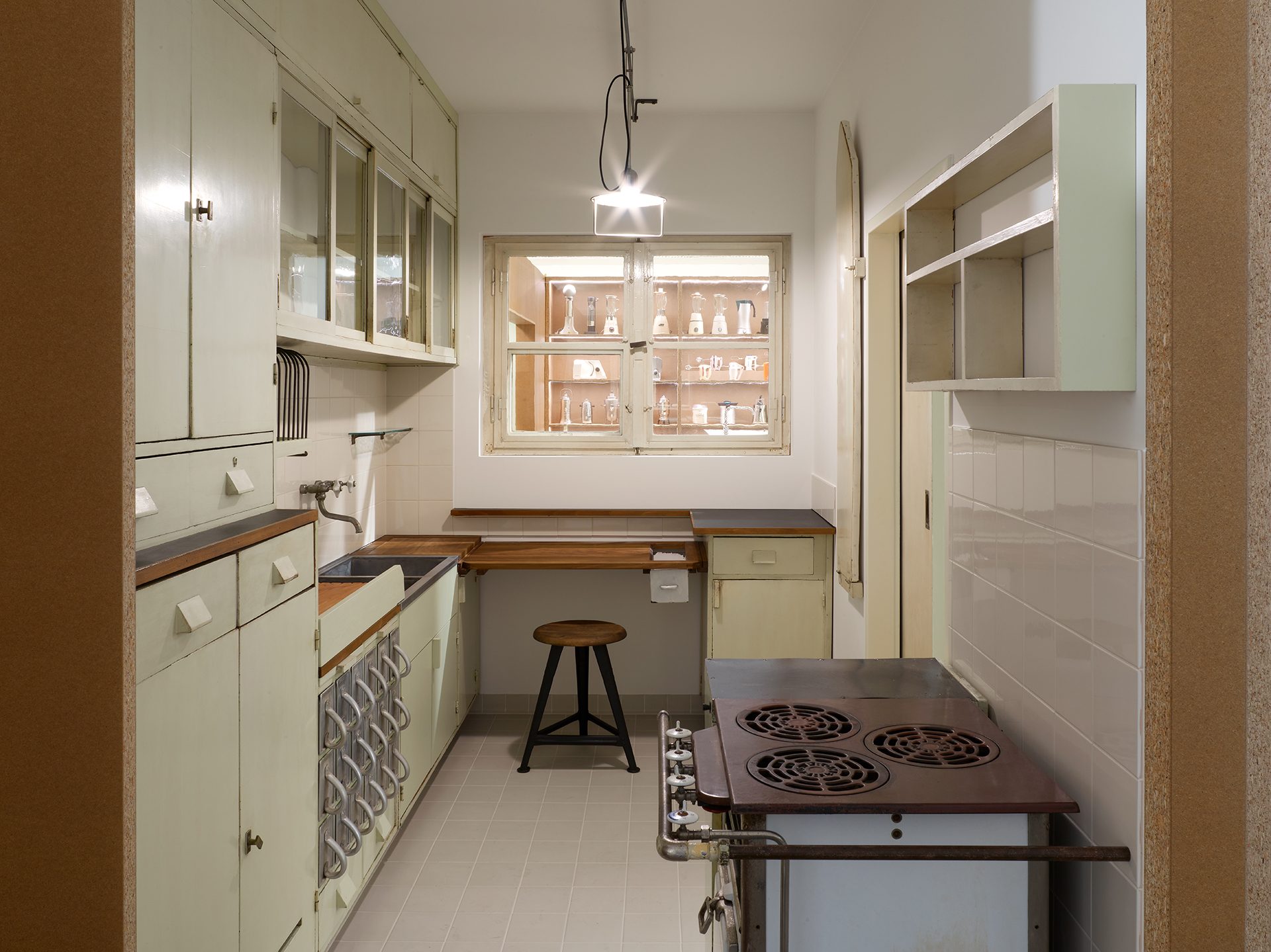 You can see the exhibition installation “Kitchen Culture” consisting of brown wall and floor elements in which various kitchens are set up.