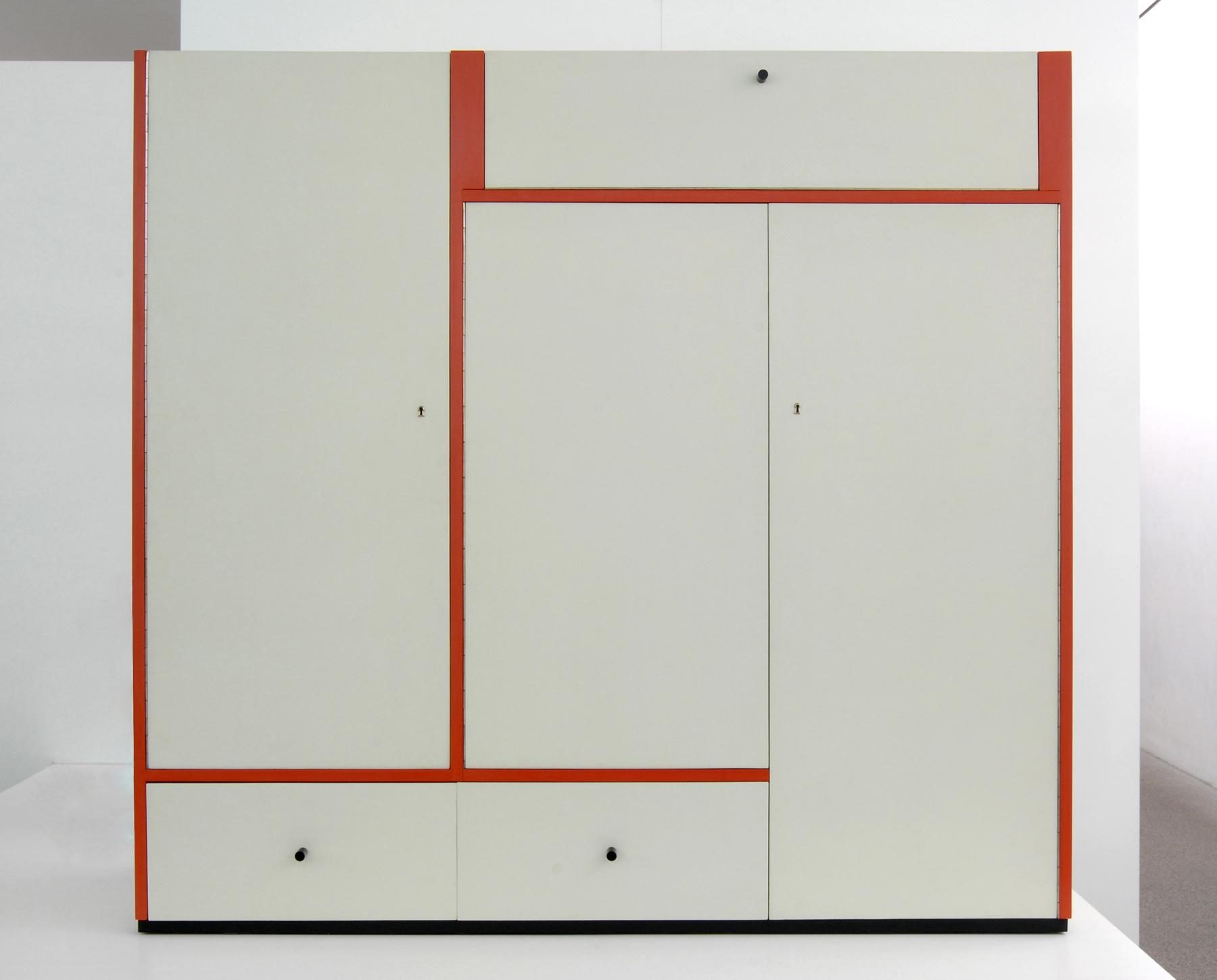 Photo of a white cabinet with two drawers at the bottom and top, with three cabinet doors in between. The elements are separated by orange lines. The small handles are black.