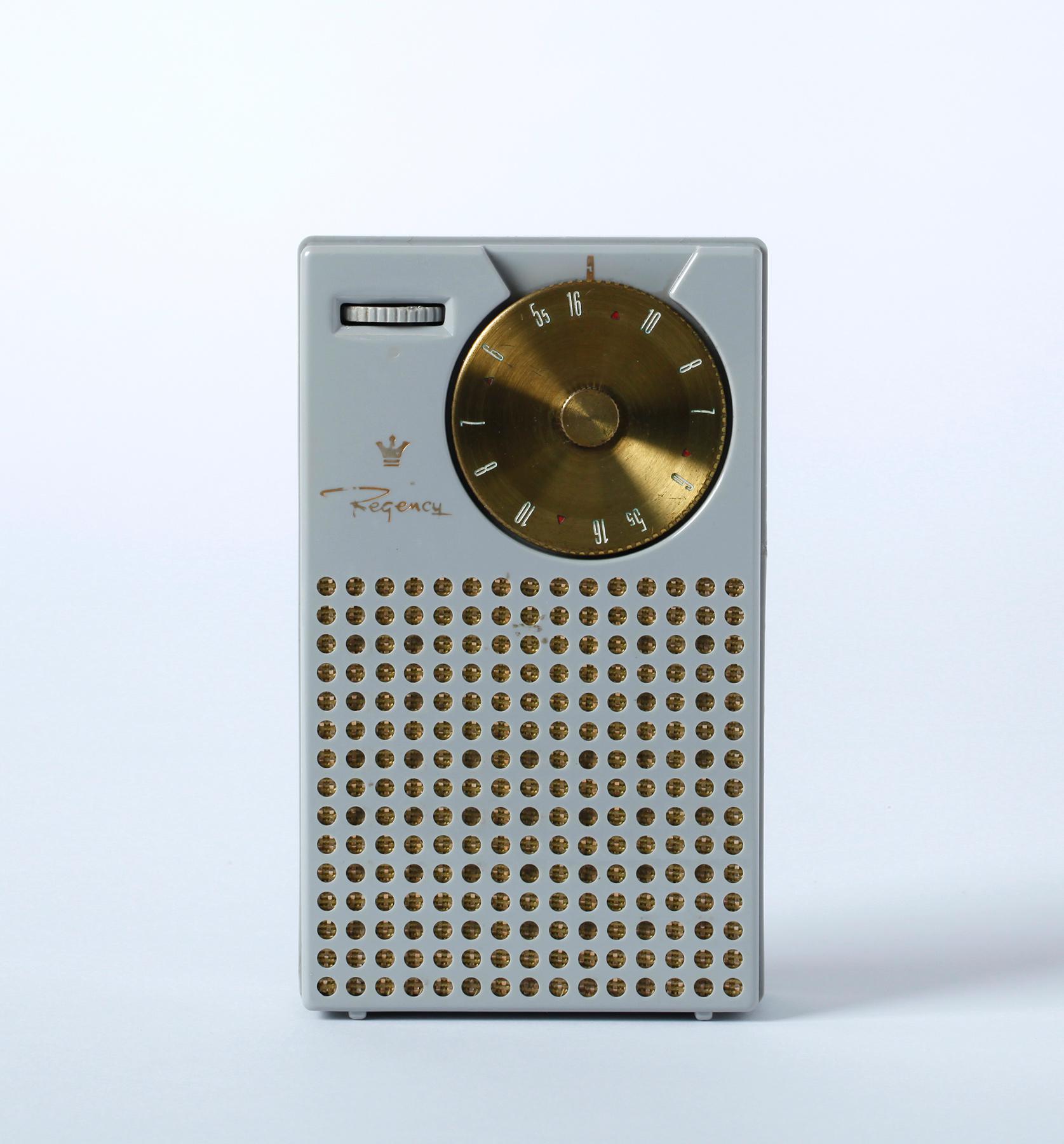 Transistor radio ‘Regency’ with light grey housing, golden frequency scale and perforated loudspeaker front.