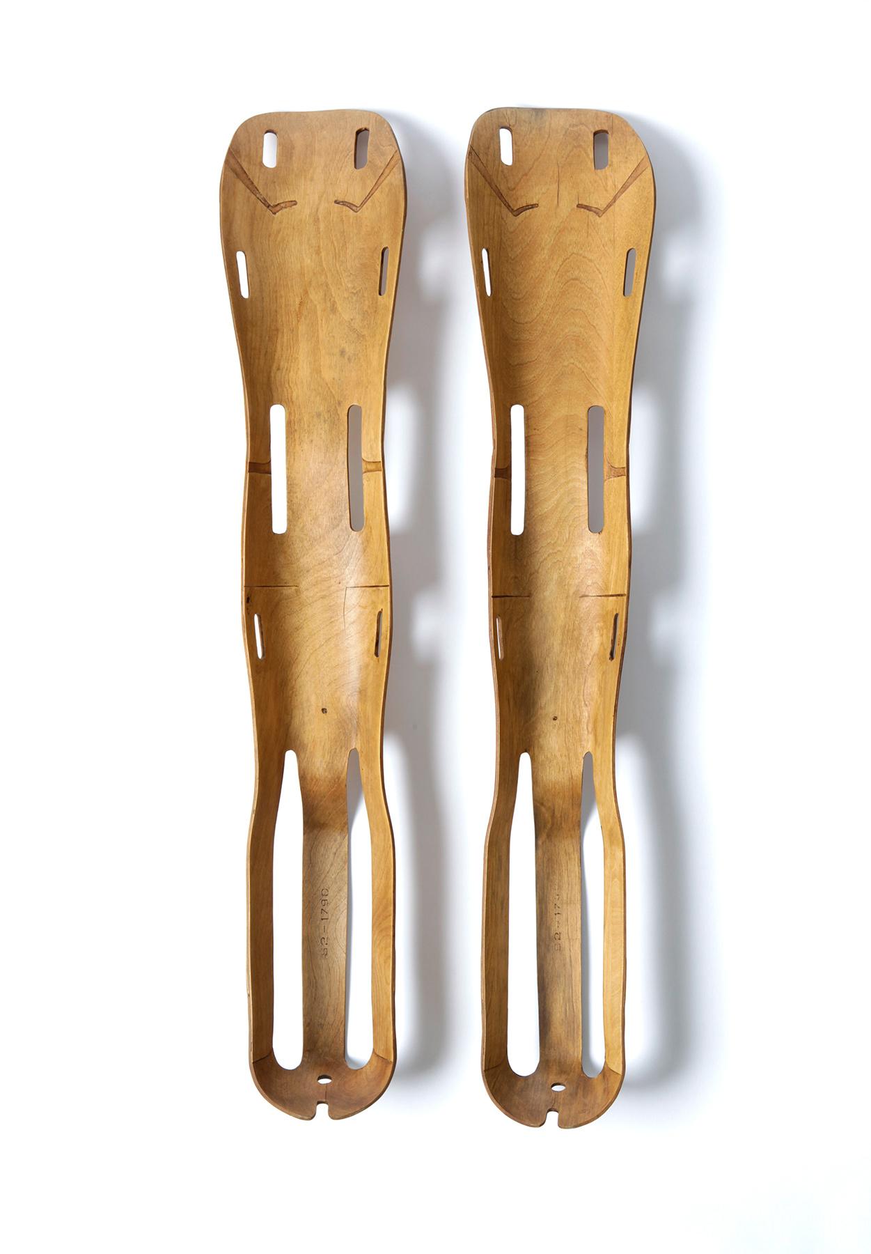 Two wooden greaves next to each other, standing upright. The rails are tapered, have holes at the top and slots at the bottom. There are smaller slits in the middle. The wood is curved like a tub.