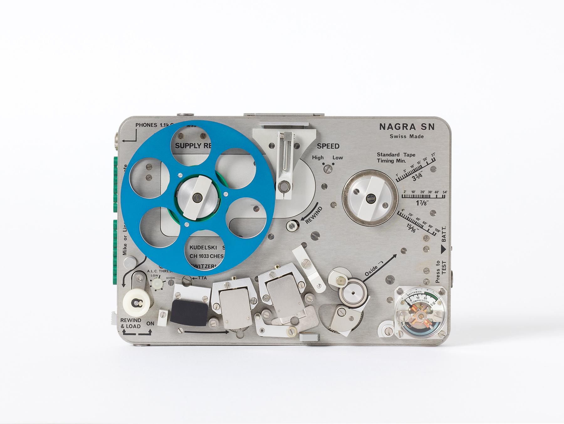 Compact, silver Nagra SN tape recorder with blue tape reel, various mechanical controls and scale displays.