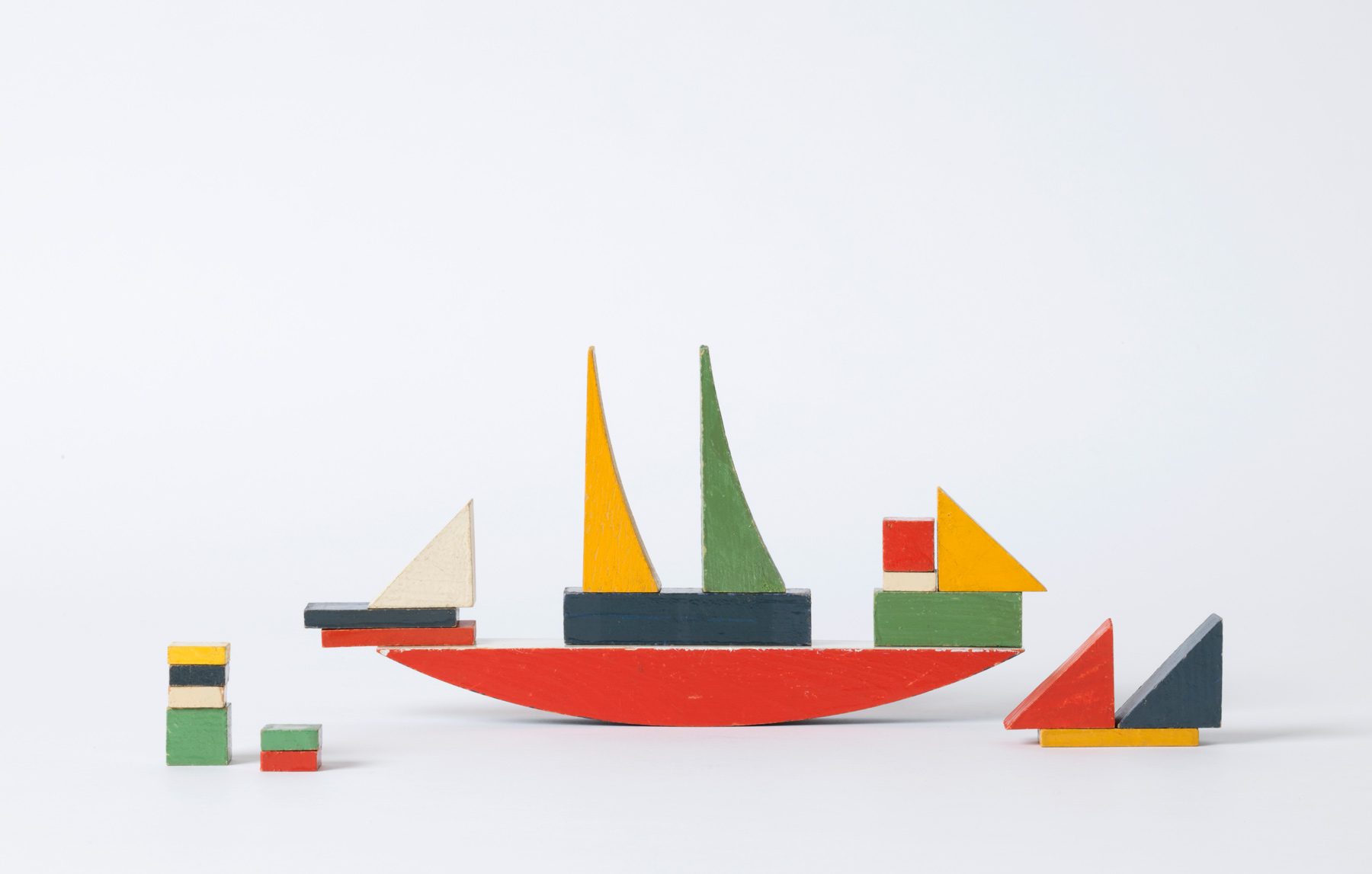 Photo of a ship made of colorful wooden blocks with two sails. Next to it is a smaller boat made of three blocks and a stack of blocks on the left.