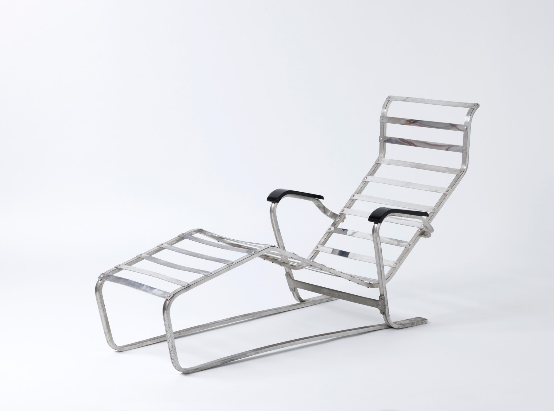 Perspective view of the metal lounger with curved frame, black armrests and a continuous strut construction.