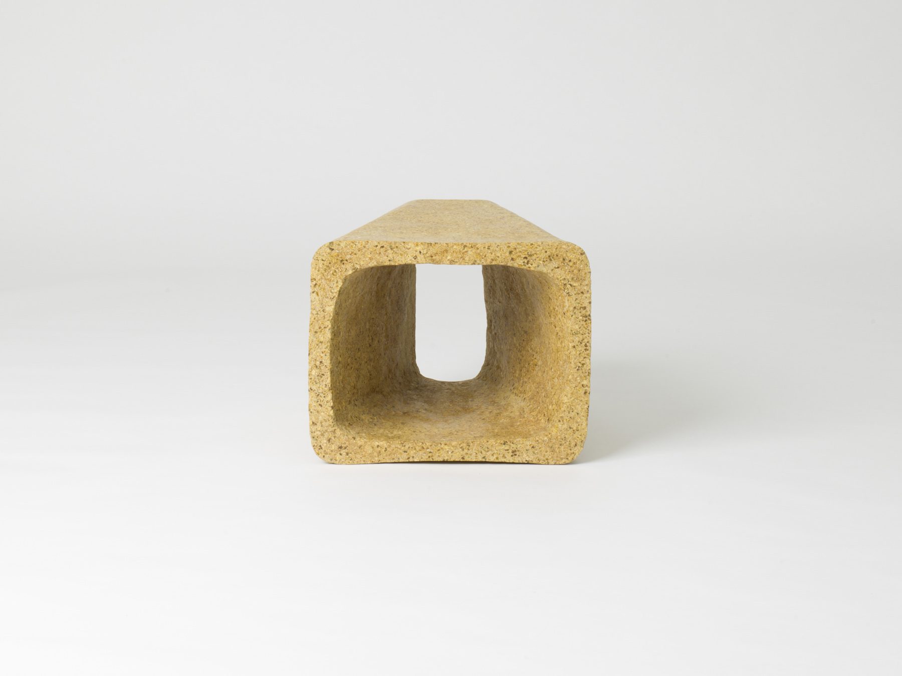 Frontal view of a hollow, trapezoidal object made of sand-coloured material.