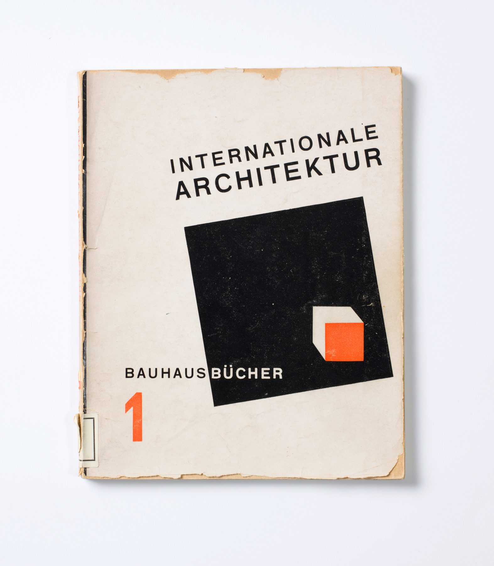 Buch Cover. Auf weißem Hintergrund steht schräg in Schwarz: Internationale Architektur. Darunter befindet sich auf einem schwarzen Quadrat ein kleiner orang-weißer Kubus. In der unteren linken Ecke steht Bauhausbücher mit einer orangen Eins.